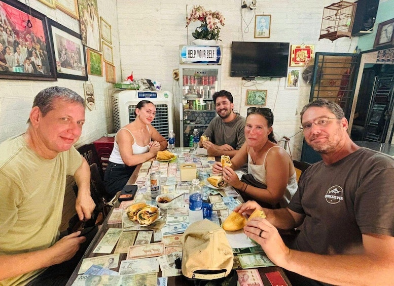 A group of people sitting around a table with food and currency notes. 4