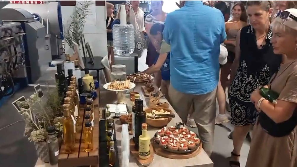 A social gathering with people standing around a table filled with food and drinks. 2