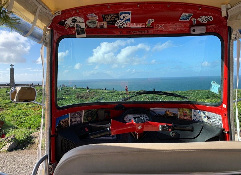 A red bus with a view of the ocean and a grassy area with a cross monument. 2
