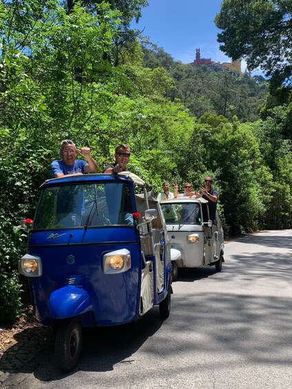 A blue and white vintage car with passengers enjoying a scenic drive through a lush, green forested area. 4