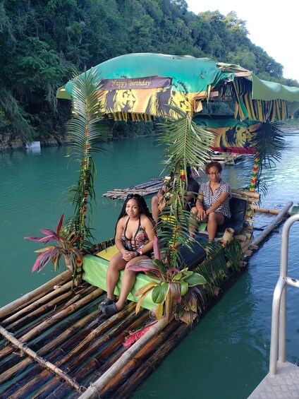 A person sitting on a bamboo raft with a 'Happy Birthday' banner, surrounded by tropical plants. 1