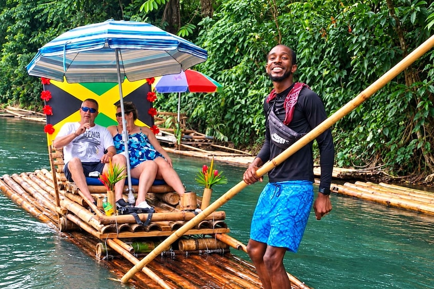 A person standing on a bamboo raft with a striped umbrella, surrounded by greenery. 2