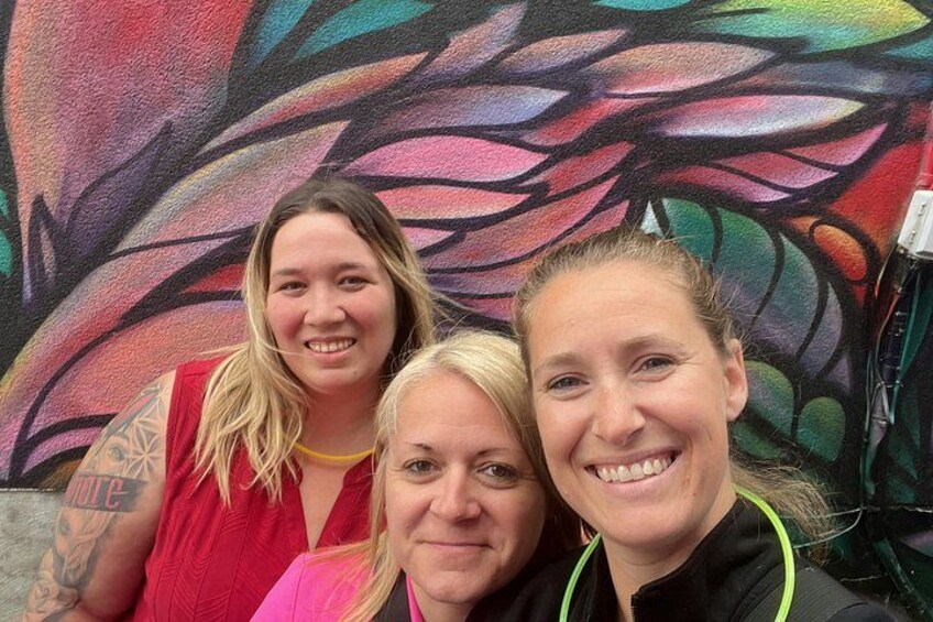 Trois personnes se tiennent devant une fresque murale aux couleurs vives. 1