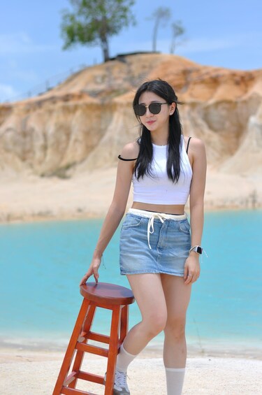 A person standing on a beach with a wooden stool, wearing a white crop top and denim shorts. 4