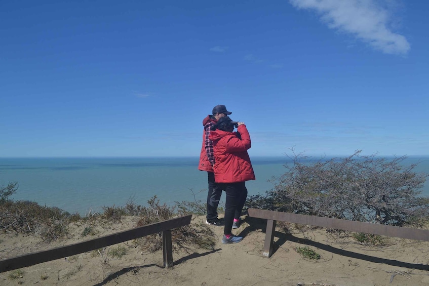 A person in a red jacket taking a photo of the ocean. 1