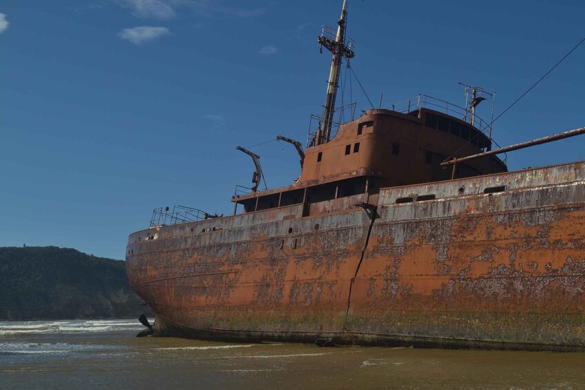 A rusted shipwreck on a beach with waves crashing against it. 4