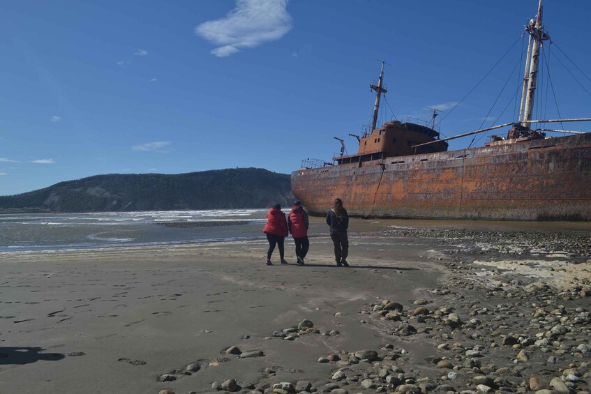 A beach with a large rusted shipwreck and two people in red jackets walking along the shore. 3
