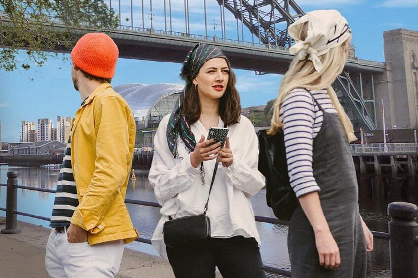Three people walking by a waterfront with a bridge in the background. 1