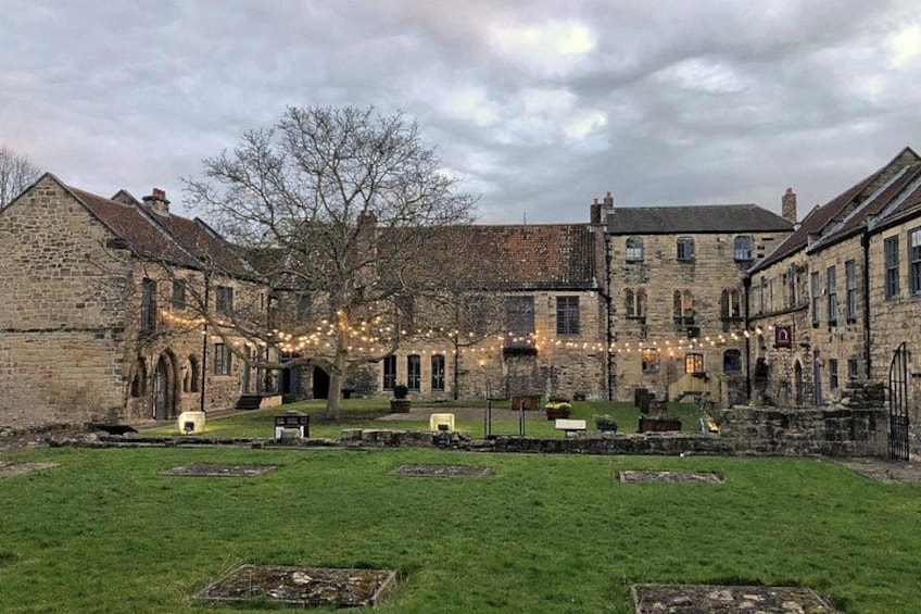 A courtyard with stone buildings, a grassy lawn, and string lights. 4