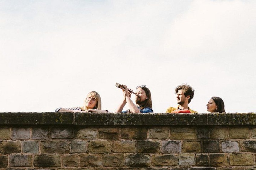 A group of people sitting on a stone wall, some looking at the sky. 5