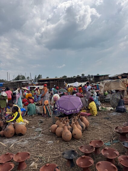 Un marché animé en plein air, où l’on voit des gens assis et debout, entourés de divers objets en céramique. 5