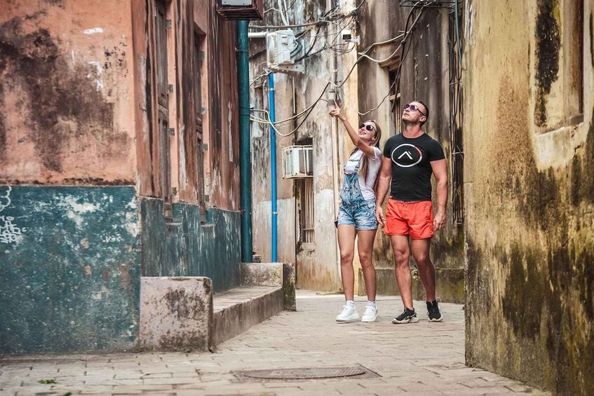 A narrow alleyway with weathered walls and a man pointing at something above. 5