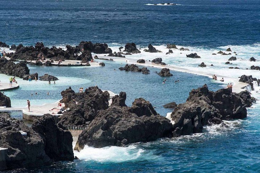 A coastal area with rocky formations, clear blue waters, and a sandy beach. 1
