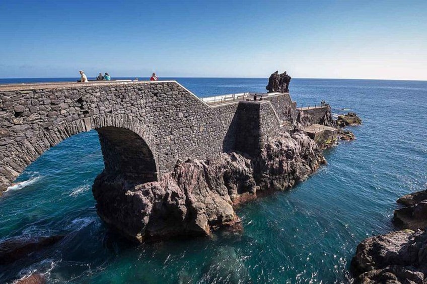 A stone bridge over water, rocky outcrops, and a clear blue sky. 5