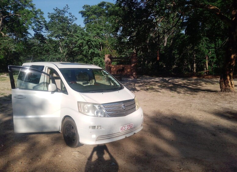 A white van parked on a dirt road with trees in the background. 1