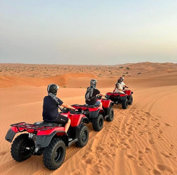 Three people riding red off-road vehicles on a sandy desert landscape. 3