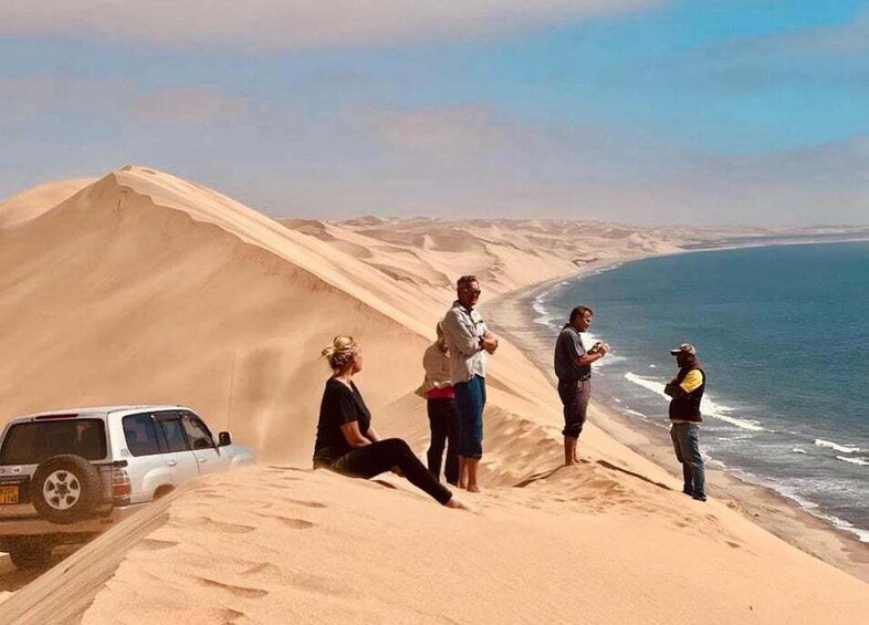 A desert landscape with sand dunes, a beach, and a white vehicle. 2