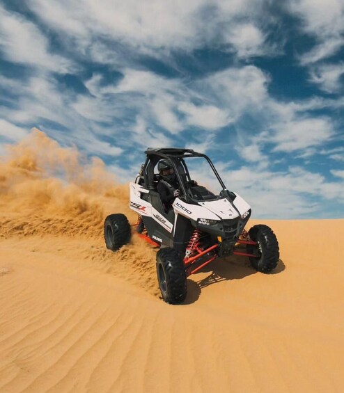 A white and black off-road vehicle with red suspension on a sandy terrain under a partly cloudy sky. 5