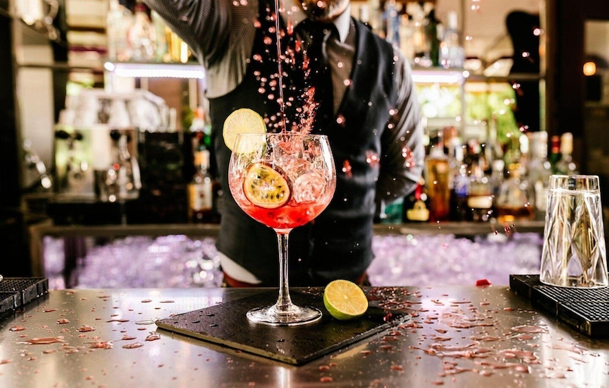 A bartender pouring a drink into a glass with a slice of lime and a slice of passion fruit. 1