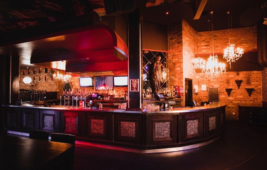 A bar with a red-lit bar counter, brick walls, and chandeliers. 4