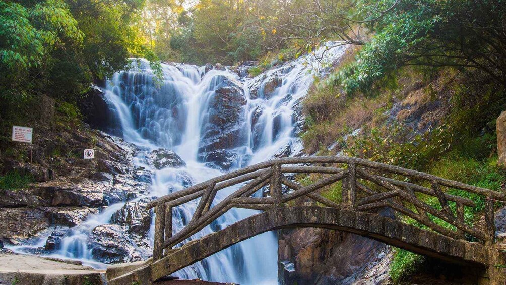 A waterfall cascading over rocks with a wooden bridge in the foreground. 4
