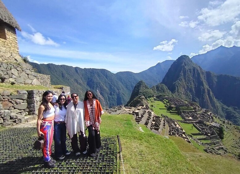 A group of people standing on a stone platform with a view of Machu Picchu ruins and surrounding mountains. 4