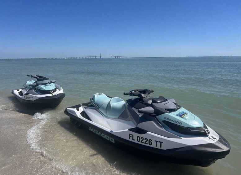 Two Sea-Doo jet skis on a beach with a bridge in the background. 1