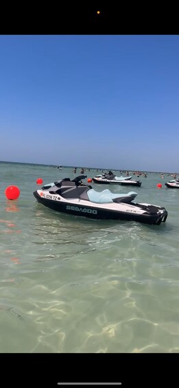 A clear blue sky over a beach with several jet skis and red buoys in shallow water. 2