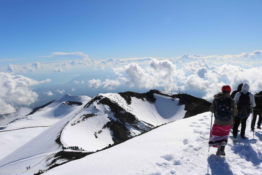 A group of hikers on a snow-covered mountain peak with a view of clouds below. 3