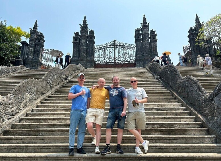A group of people standing on stone steps with ornate carvings, leading up to a gate with intricate metalwork. 3