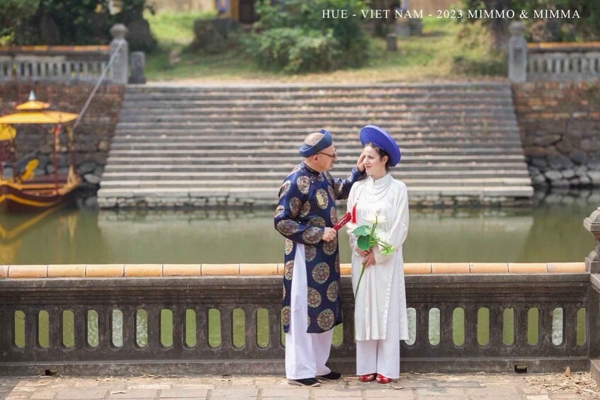 A couple in traditional attire standing by a pond with steps leading down to it. 2