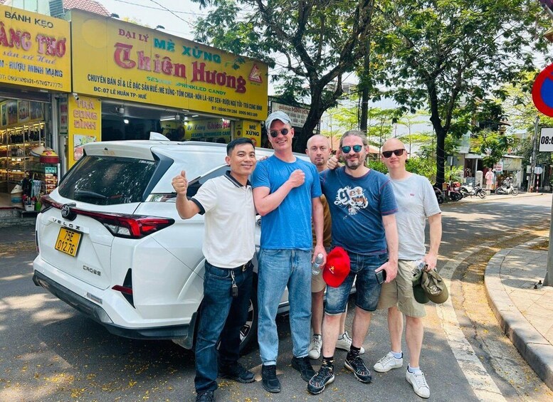 A group of people posing in front of a store with a white car parked nearby. 5