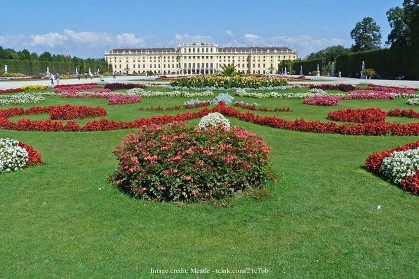 A large palace with a well-manicured garden featuring geometric flower beds and a central circular flower arrangement. 4