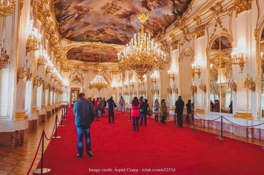 An ornate hall with a red carpet, chandeliers, and columns. 2