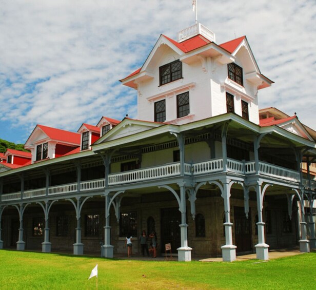 A large, white colonial-style building with red roofs and a covered veranda. 2