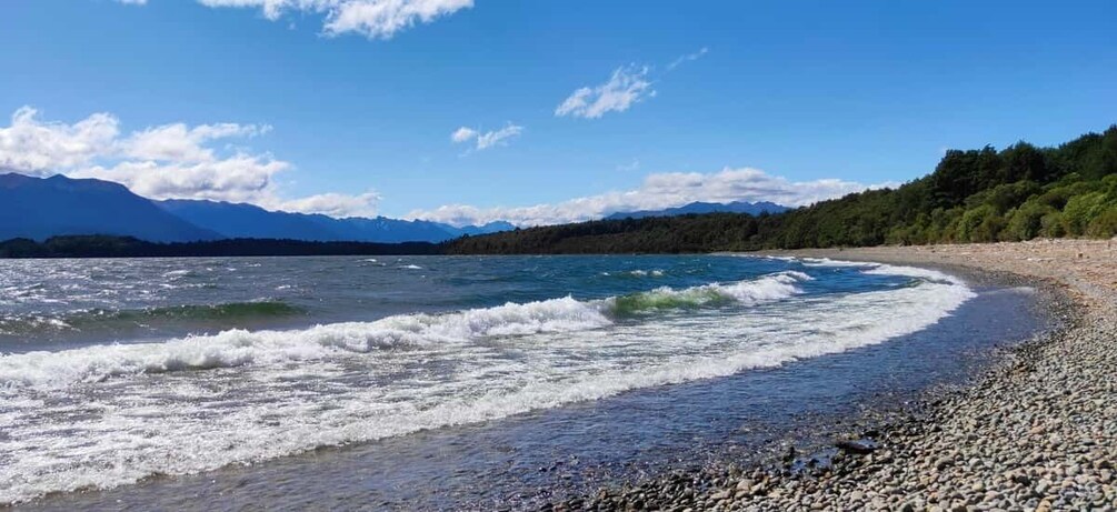 A pebble beach with waves, a clear sky, and distant mountains. 5