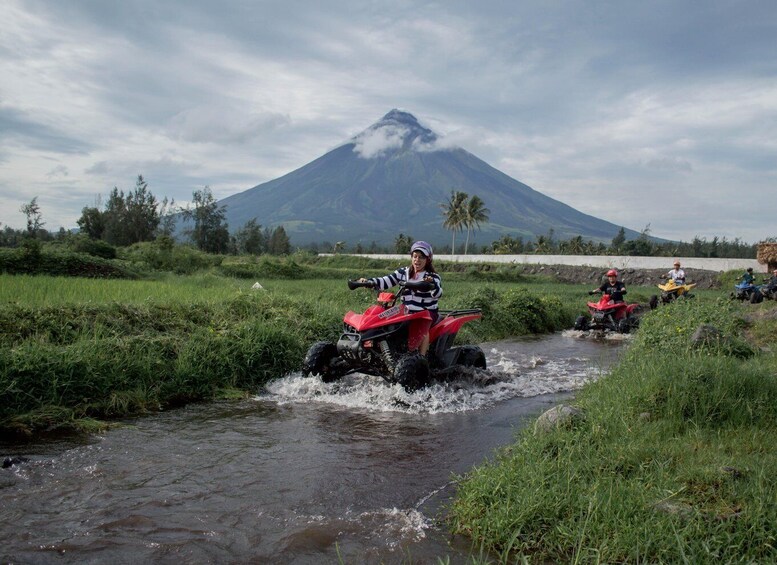 People riding ATVs through a shallow stream with a volcano in the background. 5