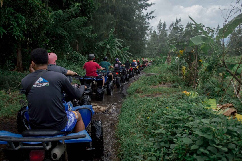 A group of people riding ATVs on a narrow, muddy path surrounded by dense tropical vegetation. 4