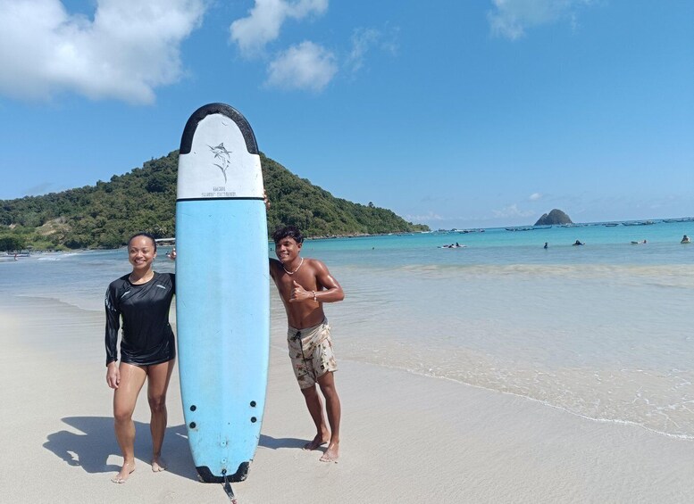 A beach with clear blue water, a surfboard, and a person standing next to it. 4
