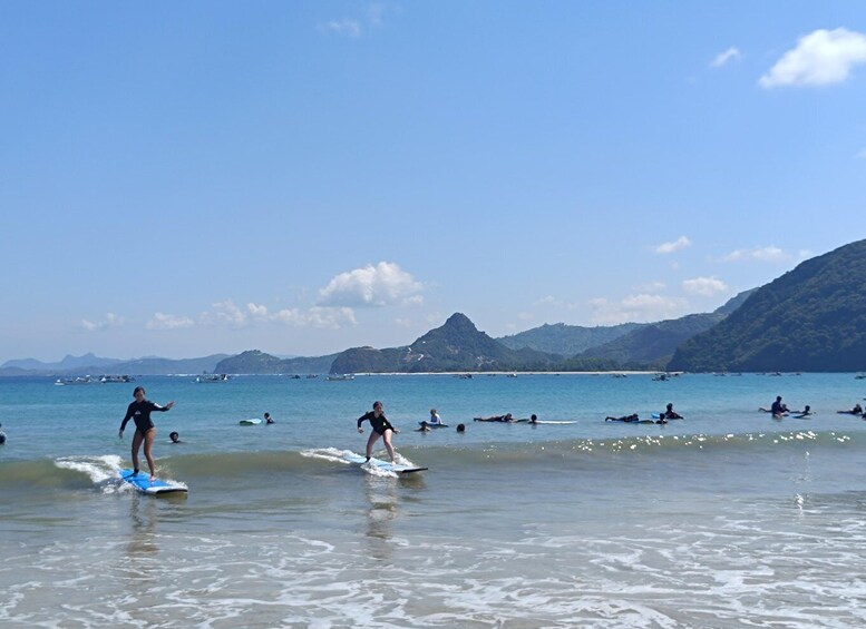 People surfing on a beach with mountains in the background. 3