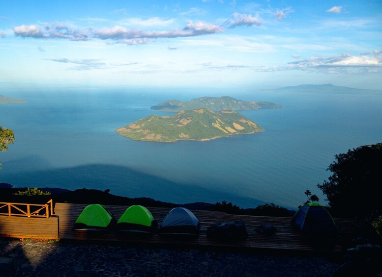 A coastal landscape with a wooden deck, three tents, and a view of a distant island. 2