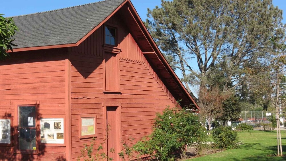 A red wooden building with a sloped roof, surrounded by trees and a grassy area. 2