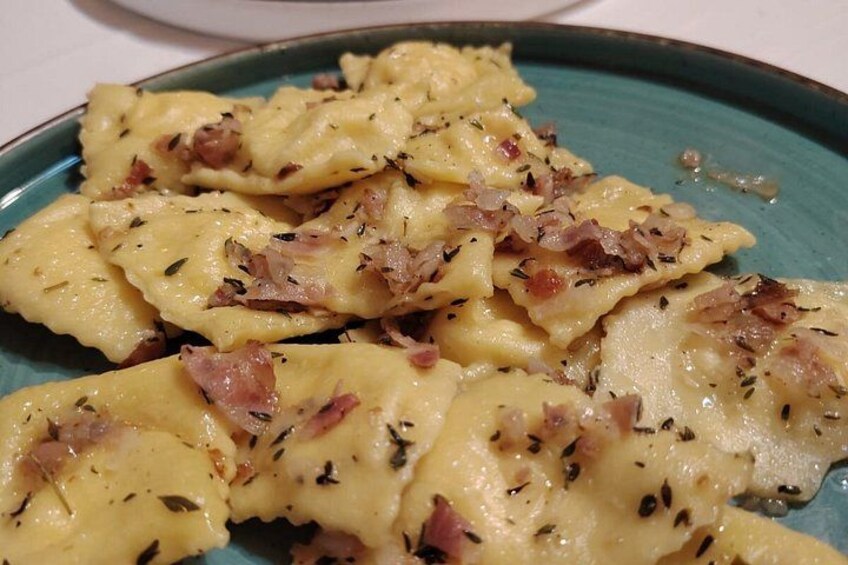 A plate of ravioli with a creamy sauce, garnished with herbs and bacon bits. 5