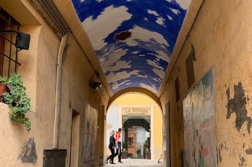 An arched passageway with a mural on the ceiling, a shop with a sign, and a potted plant. 4