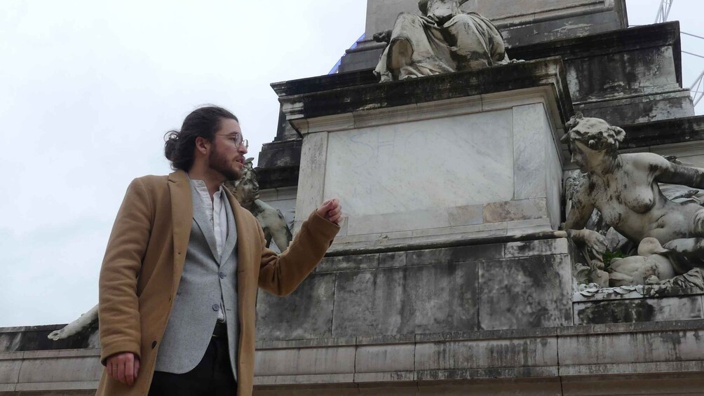 A person standing in front of a classical statue with a blank plaque. 1