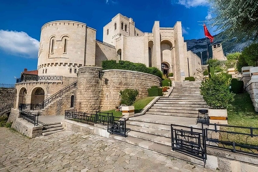 A historic stone building with a prominent tower, a flag, and a staircase leading to the entrance. 1