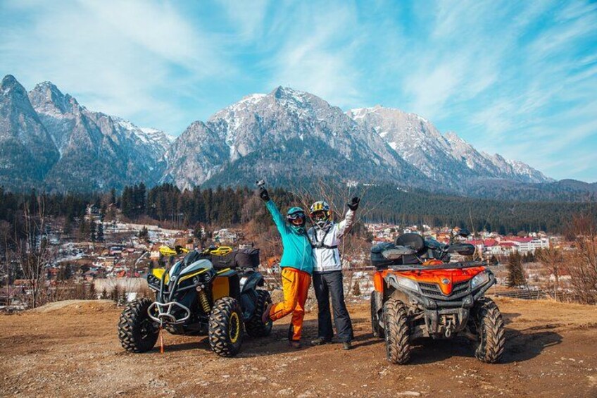 Two off-road vehicles, a person in a blue jacket, and a mountainous landscape with a town in the background. 1
