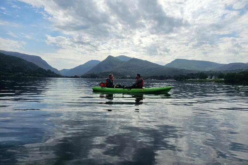 Two people kayaking on a calm lake with mountains in the background. 2