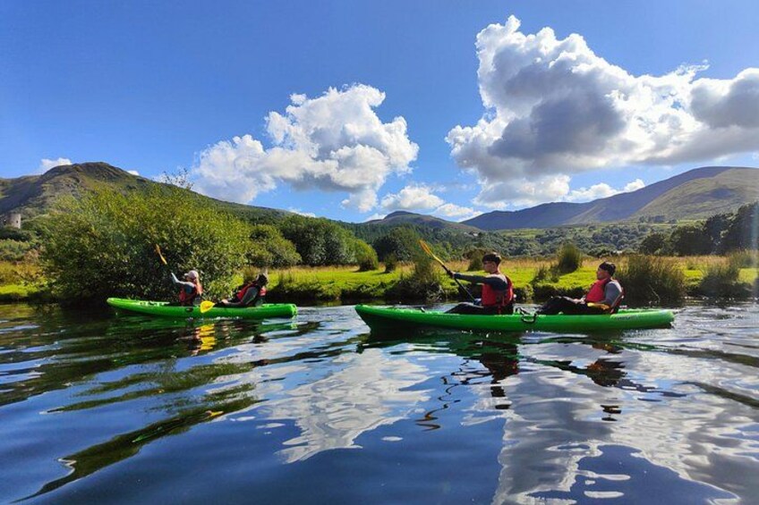 Two people kayaking on a calm river surrounded by lush greenery and hills. 5