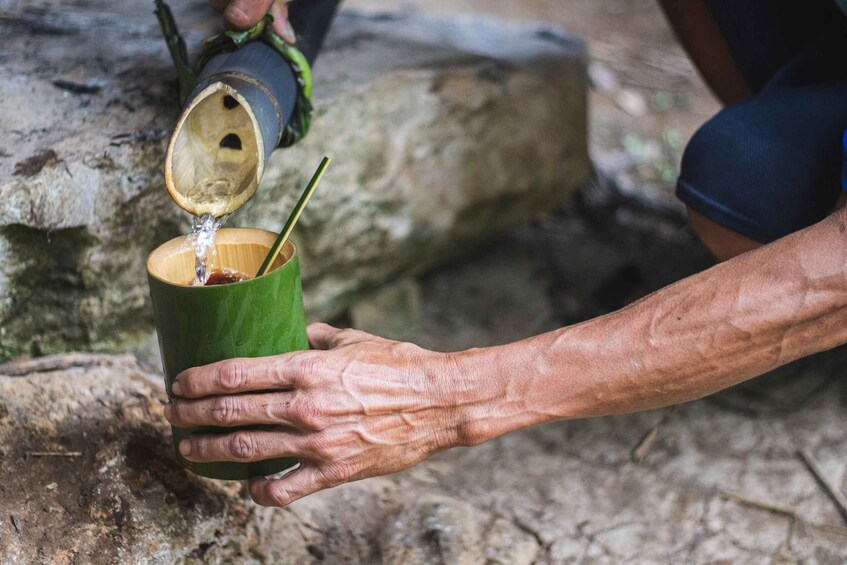 A person pouring water from a bamboo container into a green cup with a straw. 5
